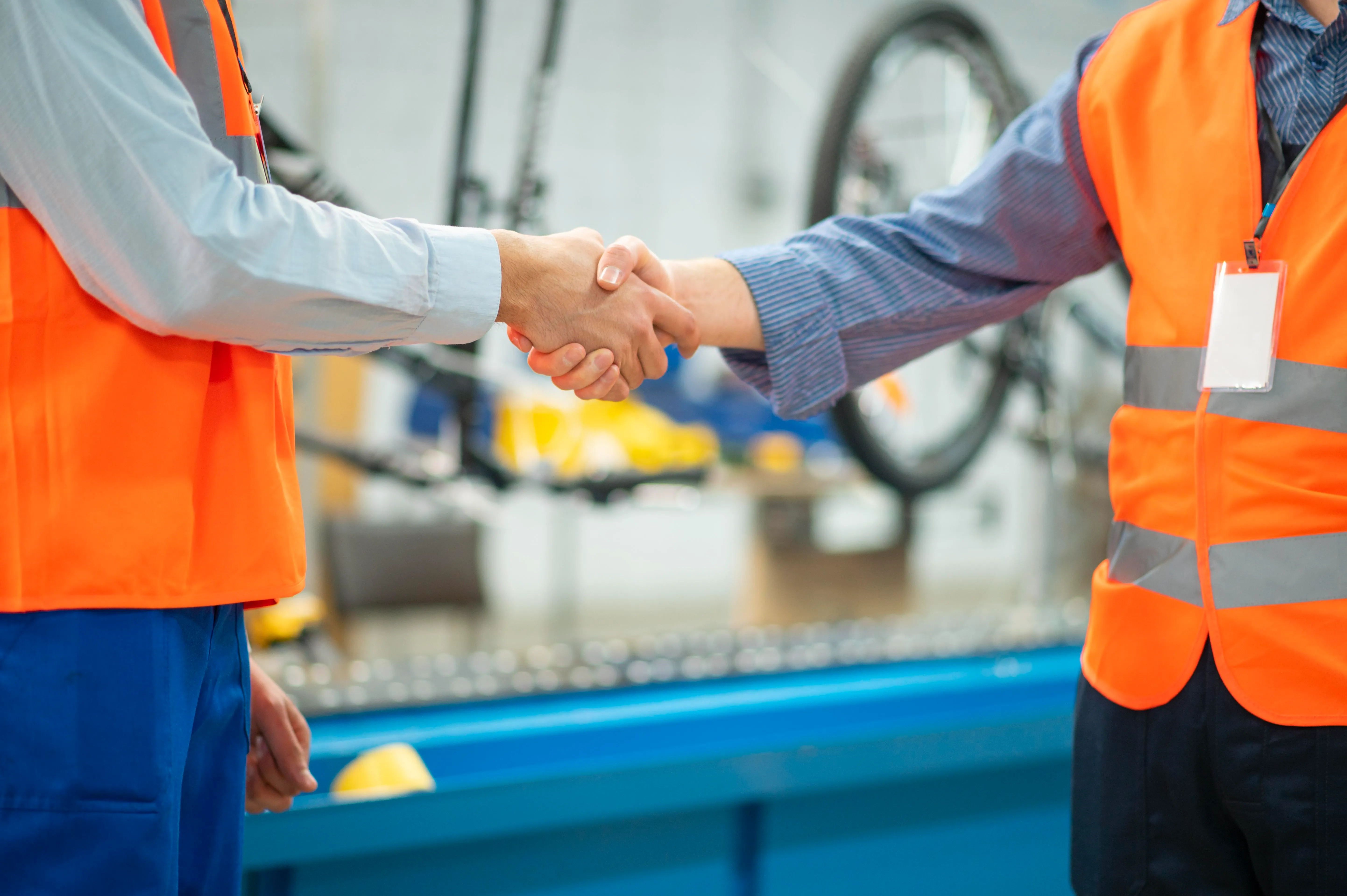 Due operatori in gilet di sicurezza che si stringono la mano, formazione sicurezza